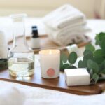 A serene spa-inspired setup featuring candles, essential oils, and eucalyptus leaves for a relaxing ambiance.